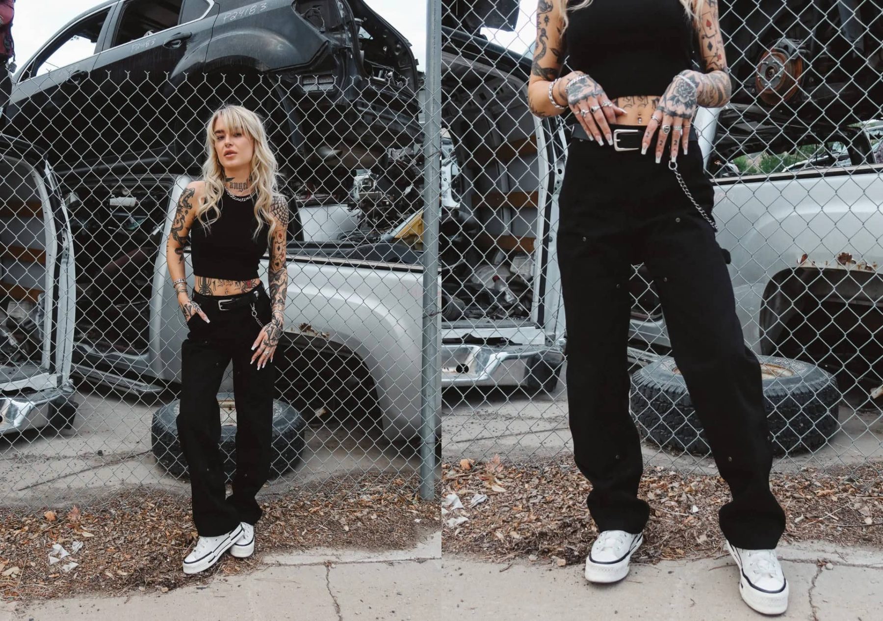 Woman in black crop top and wide-leg pants from Hell Babes standing by a chain-link fence with custom car parts in the background