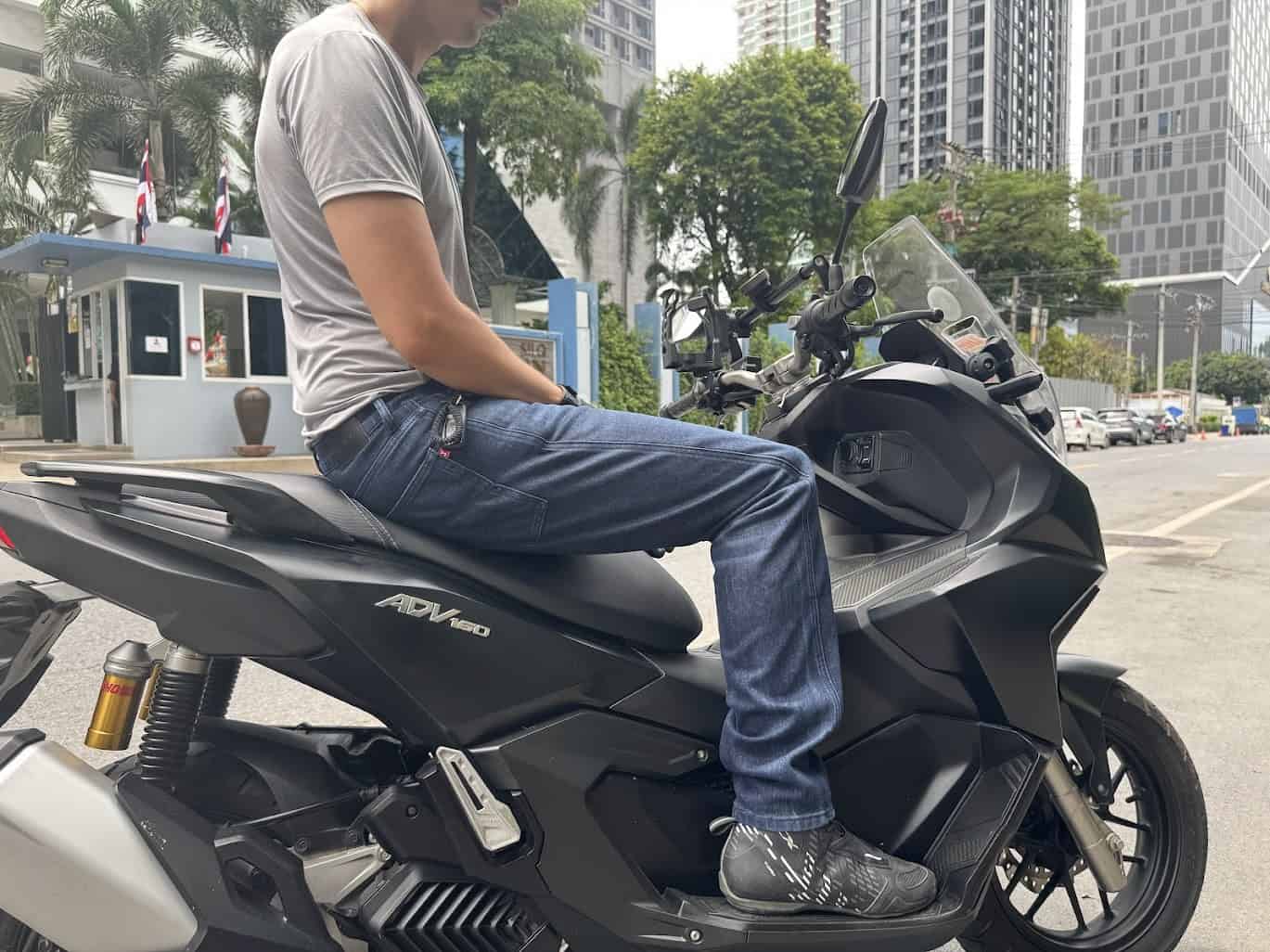 Rider wearing motorcycle boots and jeans on a Honda ADV160 scooter in the city, showing proper street riding gear and posture.