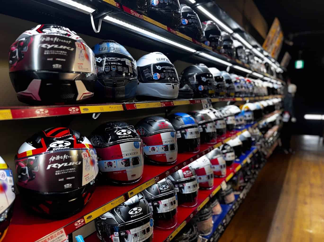 Rows of motorcycle helmets neatly displayed on store shelves, showcasing different brands, styles, and safety certifications.
