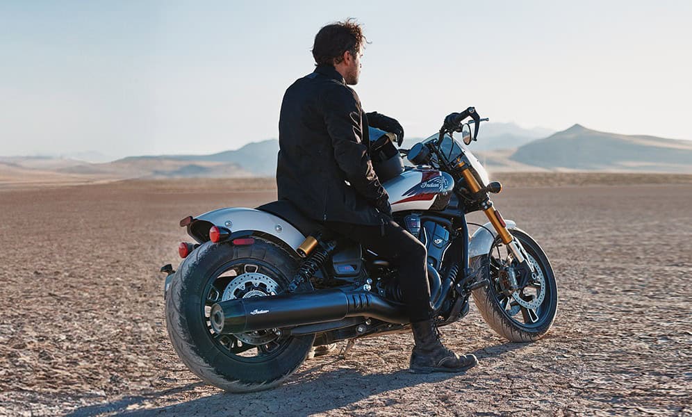 Rider sitting on an Indian 101 Scout motorcycle in a desert landscape under clear skies