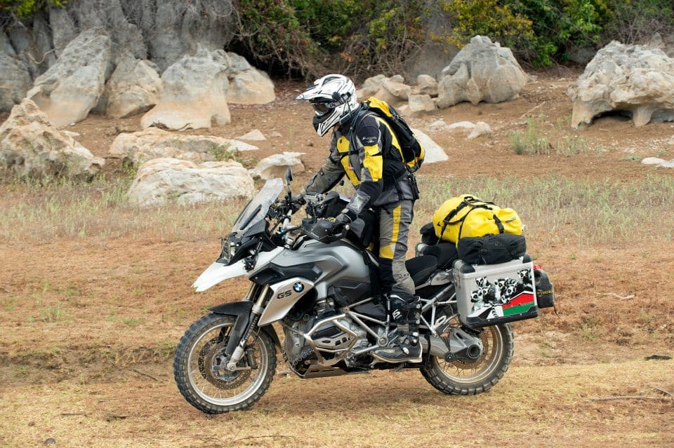 Rider on a BMW GS adventure motorcycle tackling rocky terrain with full touring gear and luggage.