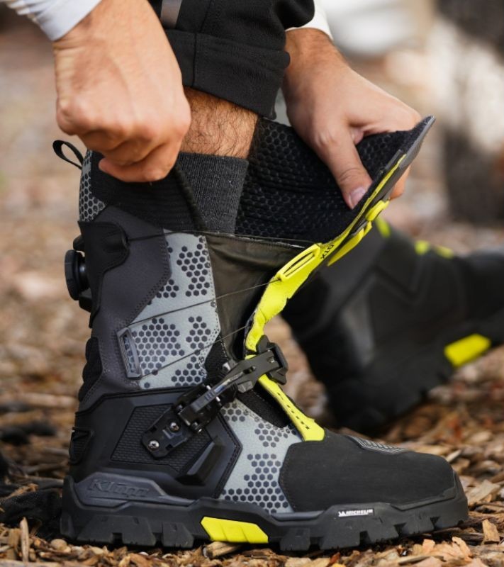 Rider tightening Klim Adventure GTX boots with BOA and buckle system, showing rugged design and Michelin outsole.
