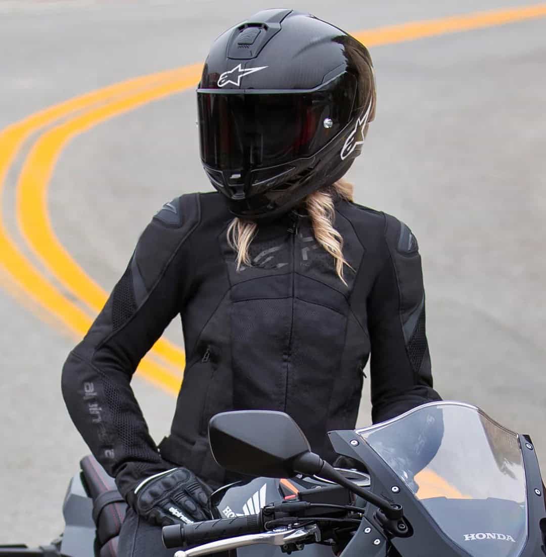 Woman wearing the Alpinestars Stella T-GP Plus R V4 Airflow jacket and helmet, showing mesh textile construction for hot-weather protection.