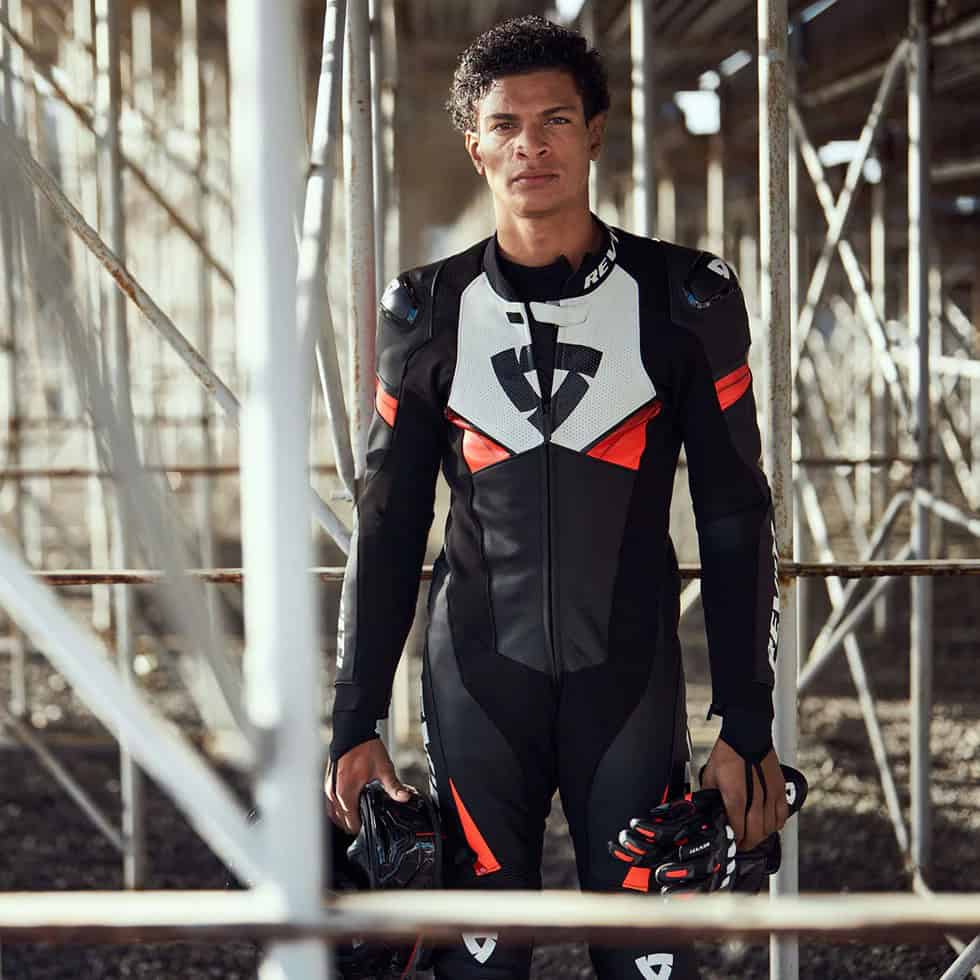 Rider wearing the REV’IT! Argon 2 race suit, showcasing its perforated leather panels, flexible stretch zones, and bold red-white-black design.