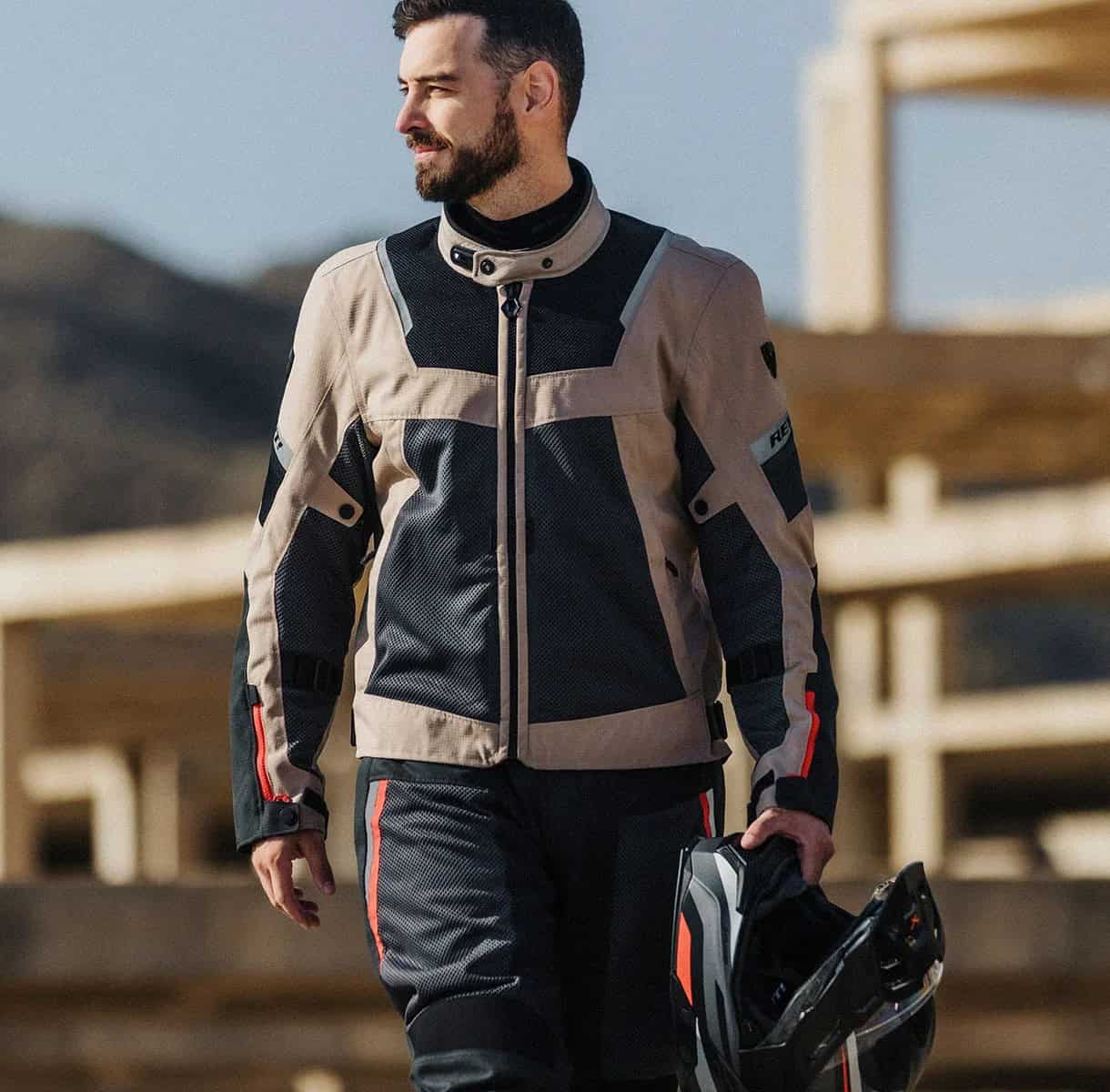 Rider wearing REV’IT Tornado 4 H2O Pants and jacket, holding a helmet while standing outdoors on a sunny touring day.