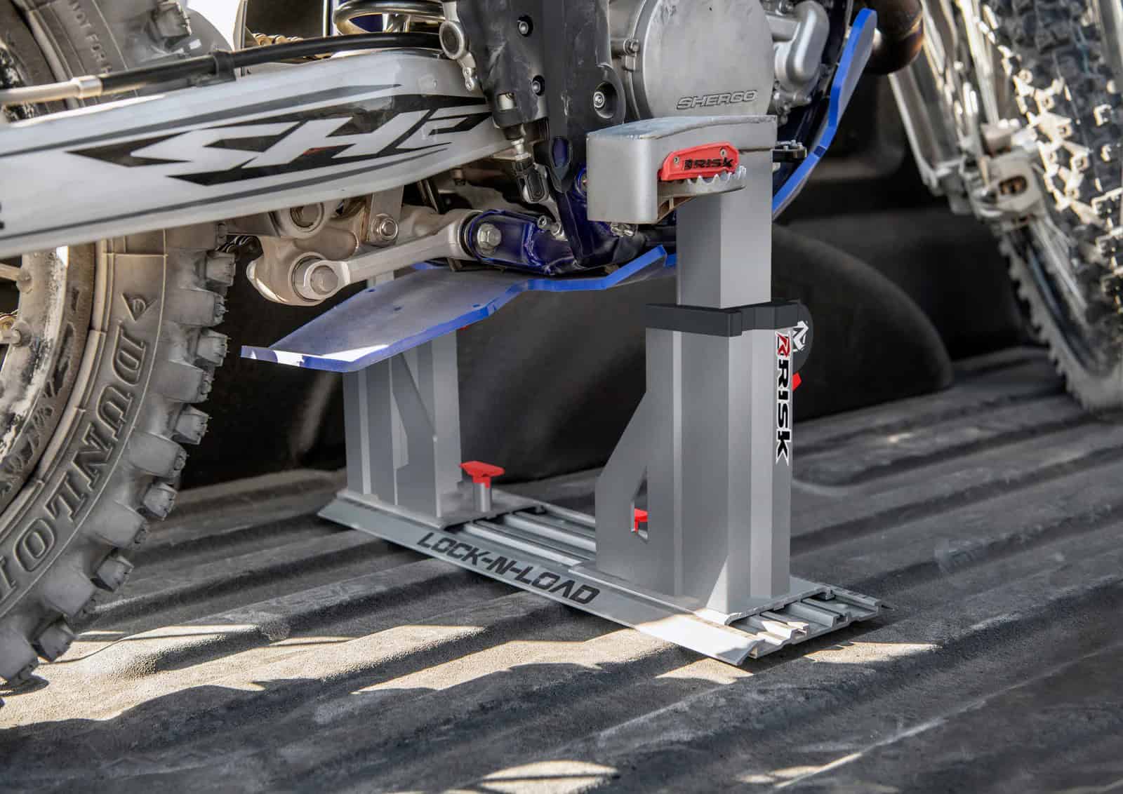 A dirt bike secured by the footpegs in a Risk Racing Lock-N-Load Pro HD strapless transport system mounted in a truck bed.