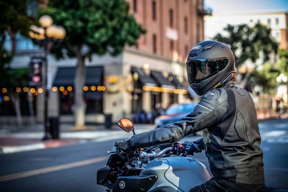 Motorcyclist wearing a Shoei RF-1400 helmet and leather jacket riding through an urban street, highlighting its compact design and aerodynamic fit.