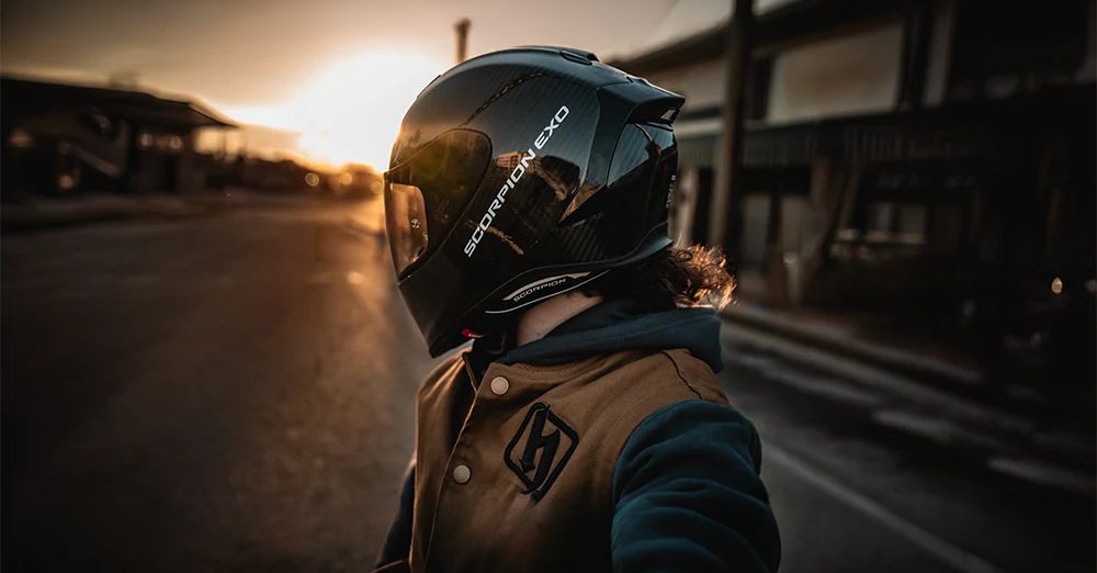 Rider wearing a Scorpion EXO-R1 Air helmet in black, facing sunset on an empty street, showcasing its sleek aerodynamic design.