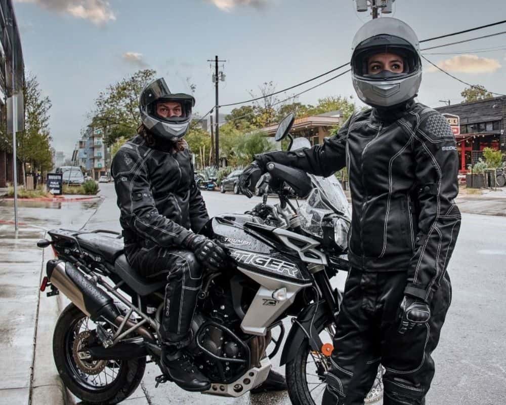 Two riders in black Sedici Alexi 2 Mesh Pants and jackets on Triumph Tiger motorcycles during a rainy city ride.