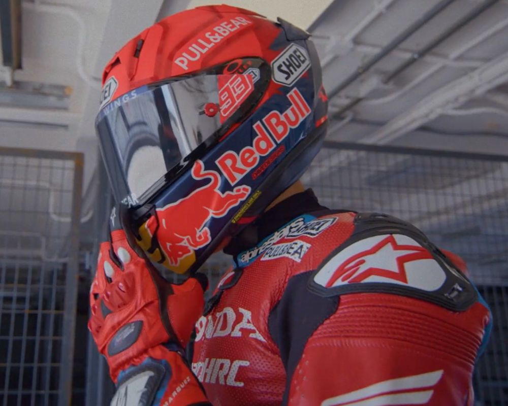 MotoGP racer wearing a Shoei X-15 helmet in Red Bull livery, captured in the paddock adjusting the fit before a high-speed run.