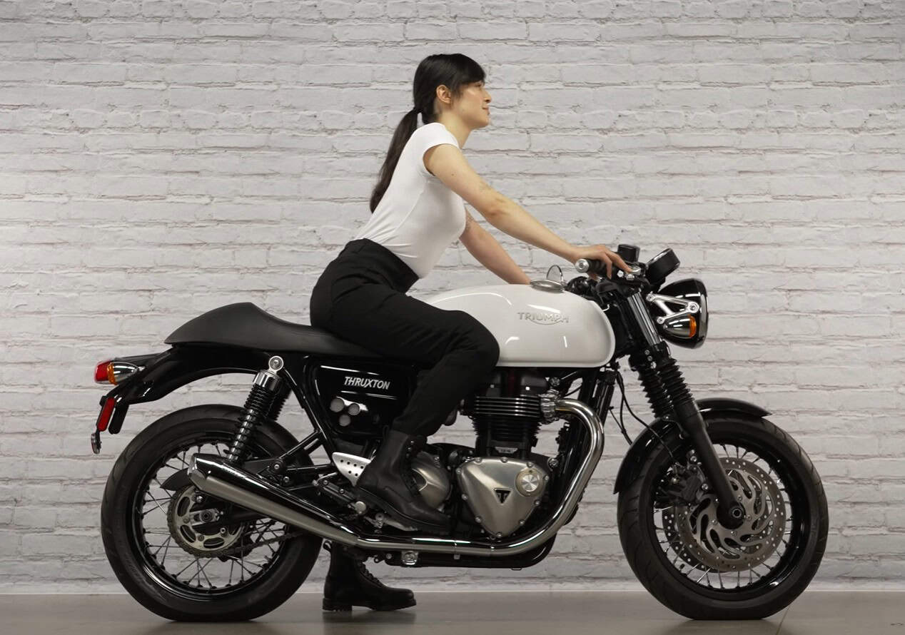 Woman seated on a Triumph Thruxton motorcycle wearing Street & Steel Moto Leggings, showing their high-rise fit and sleek riding posture.