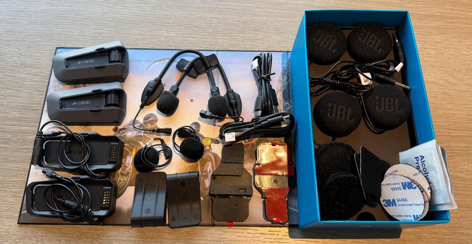 Cardo Packtalk Edge dual-pack set laid out with head units, JBL speakers, microphones, mounts, and accessories on a table.
