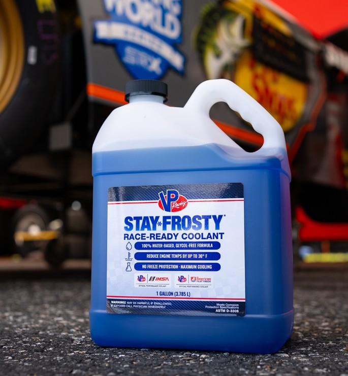 VP Racing Stay Frosty Race Ready Coolant bottle placed on asphalt near a race car in pit area