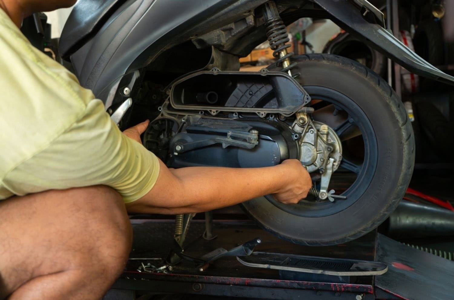 Mechanic working on a scooter rear wheel using the built-in center stand