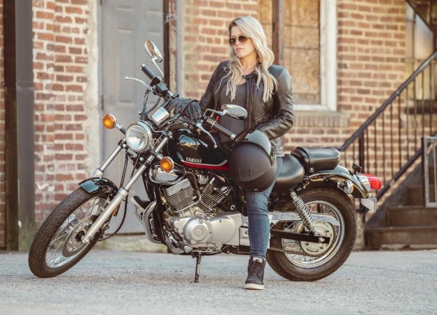 Woman standing beside a Yamaha V Star 250 cruiser holding a helmet in an urban setting