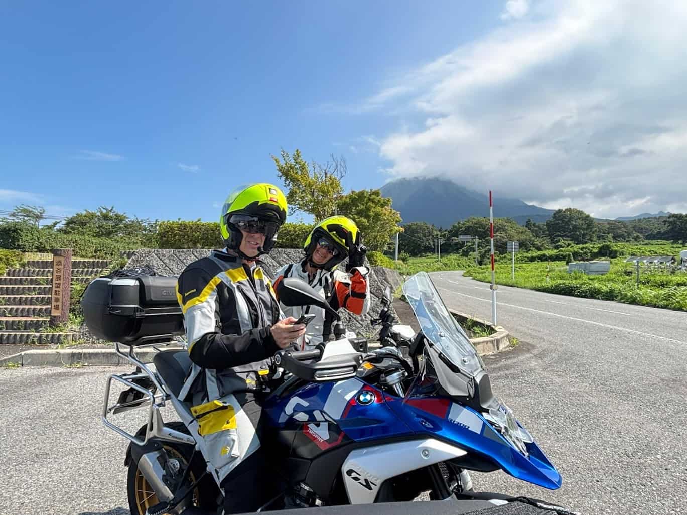 Two motorcyclists in bright helmets smiling during a scenic weekend ride, symbolizing pay-per-mile insurance and low-mileage savings.