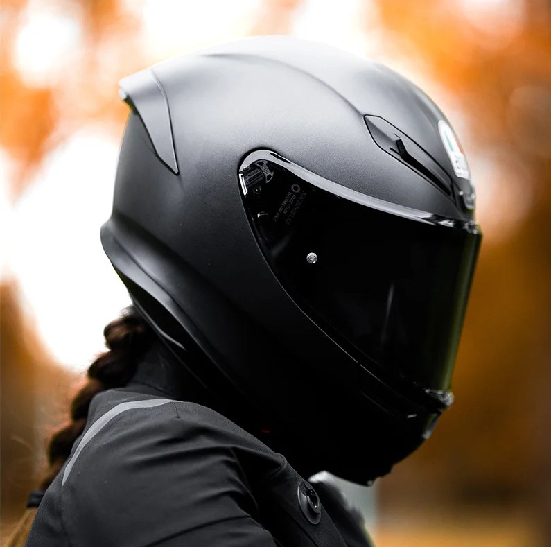 Close-up of a rider wearing a matte black AGV K6 S full-face helmet with tinted visor, showcasing its sleek aerodynamic design.