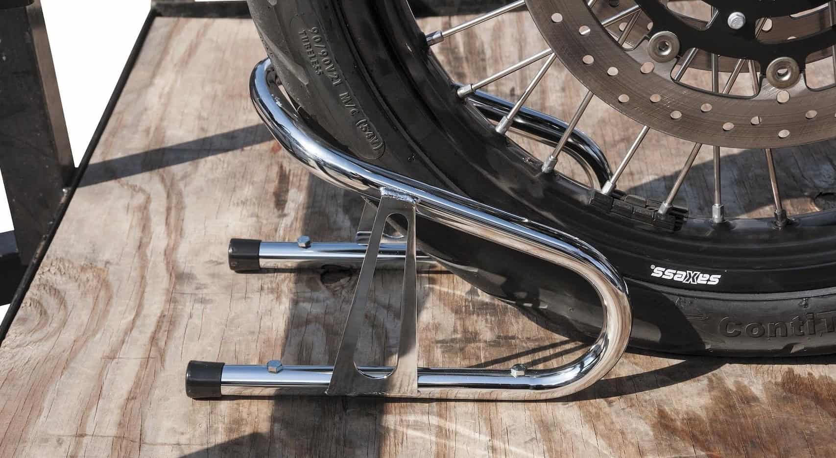 Close-up of a motorcycle front wheel secured in a chrome BikeMaster Wheel Chock mounted on a wooden trailer floor.