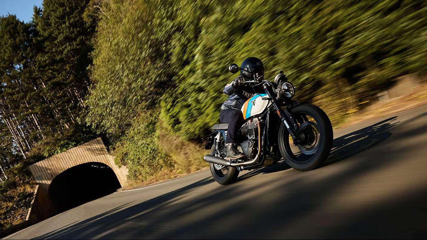 Rider leaning into a turn on a Triumph Speed Twin 900 motorcycle near a forest tunnel