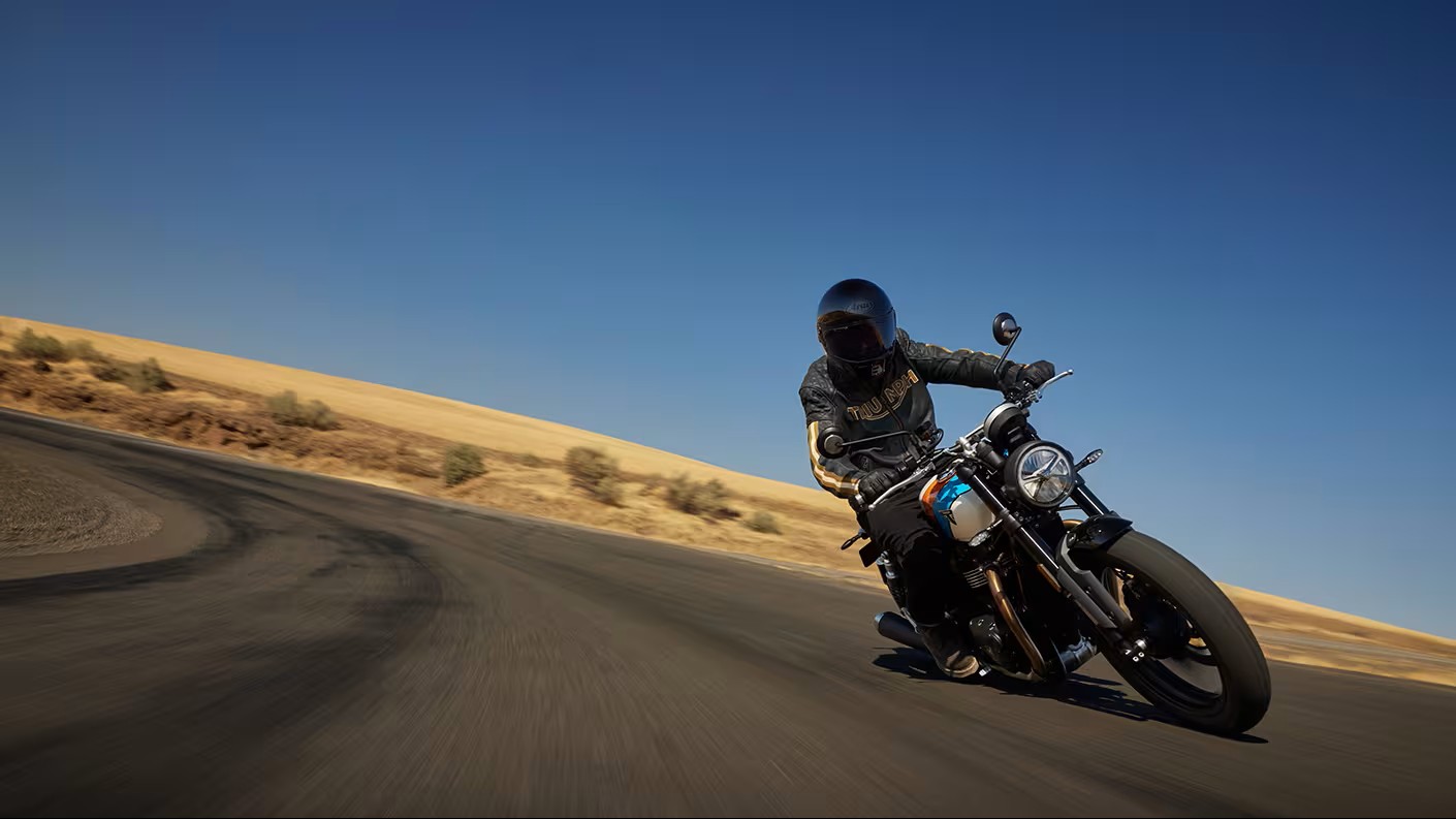 Rider leaning into a curve on a Triumph motorcycle under a clear blue sky, showcasing balance and control