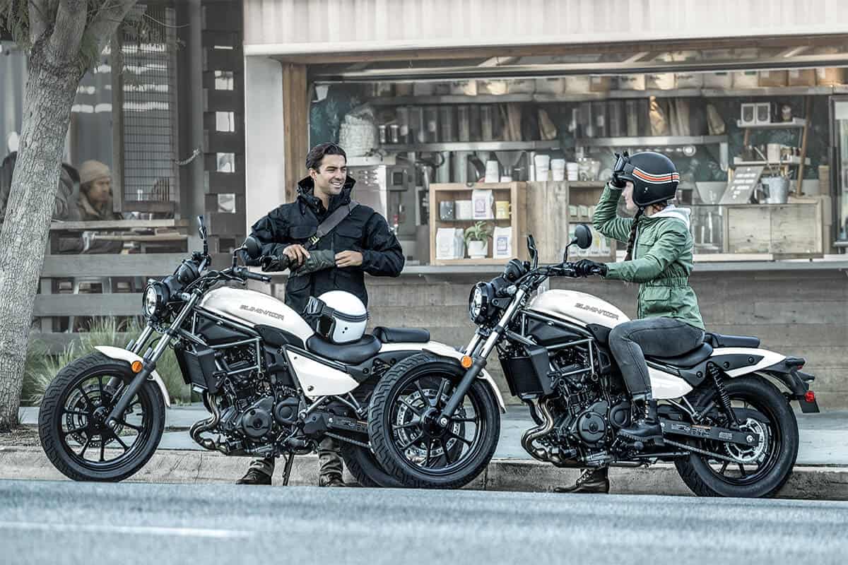 Two riders chatting beside their motorcycles outside a café, preparing for a test ride and adjusting gear