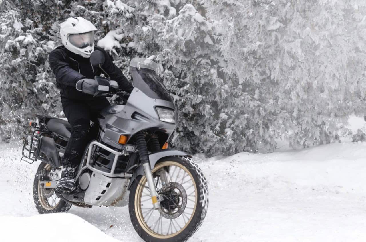 Motorcyclist riding through snow-covered forest on an adventure bike, testing winter gear fit and adjustability in freezing conditions