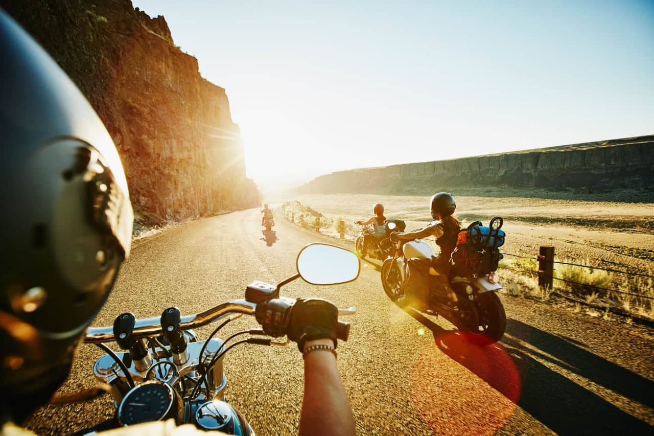 Group of motorcyclists riding through a scenic desert canyon at sunrise, capturing the freedom and heat of summer rides.
