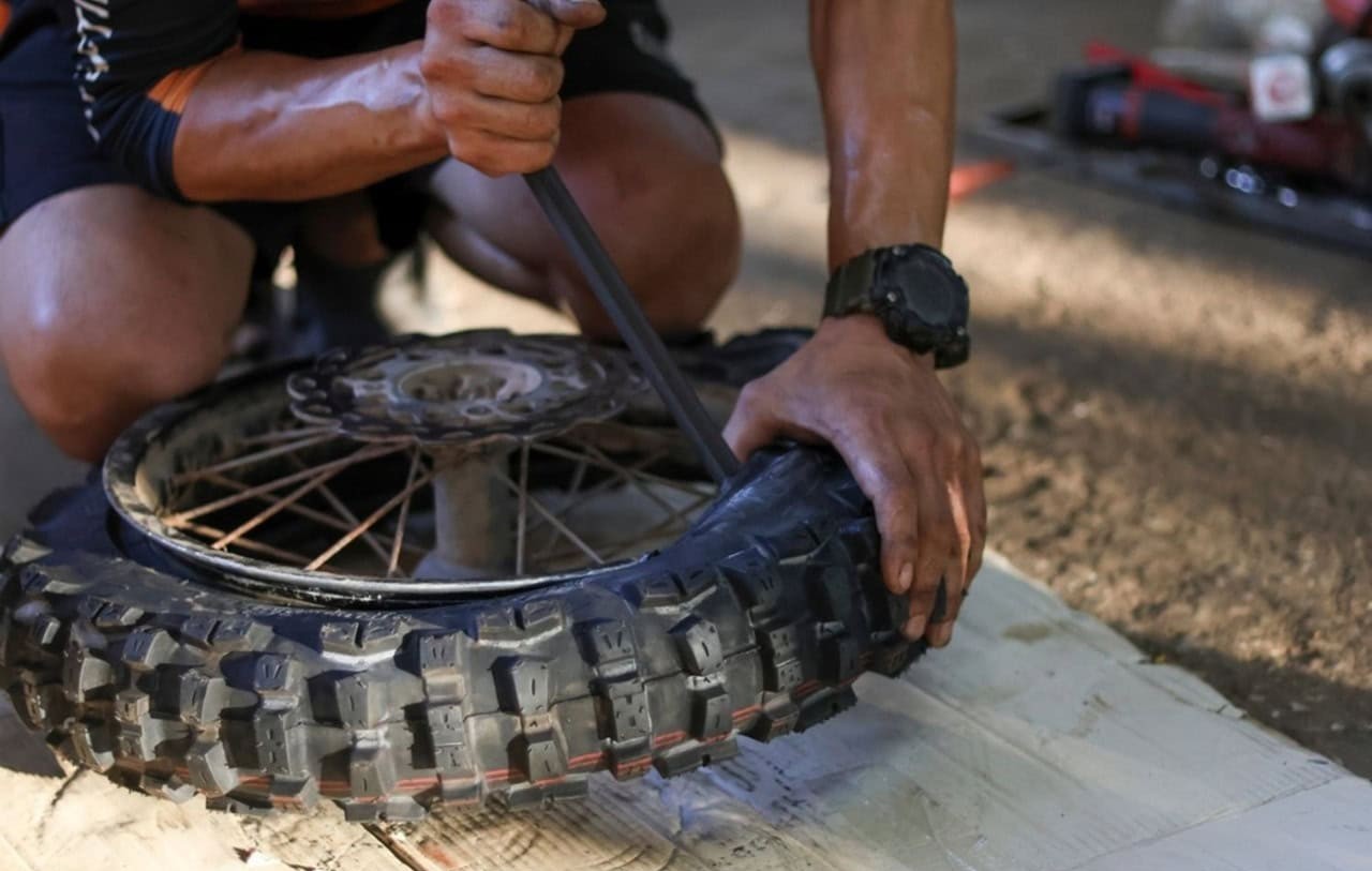 Close-up of a rider using tire irons to mount a dirt bike tire, showing hands-on maintenance work.