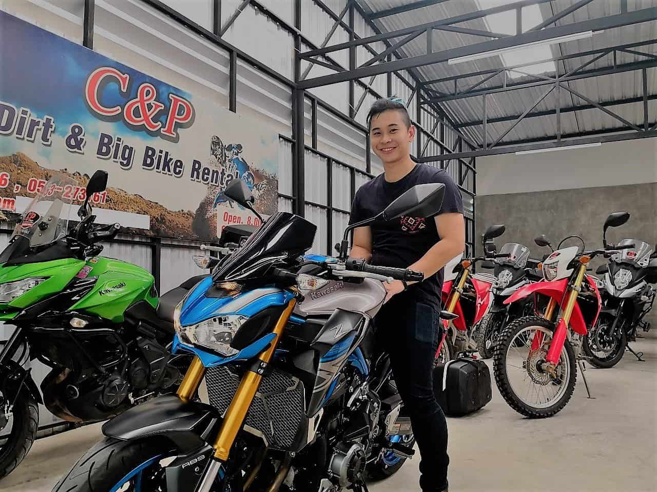 Owner at C&P Big Bike Rental in Chiang Mai standing beside a Kawasaki Z900, surrounded by adventure and touring motorcycles in the shop