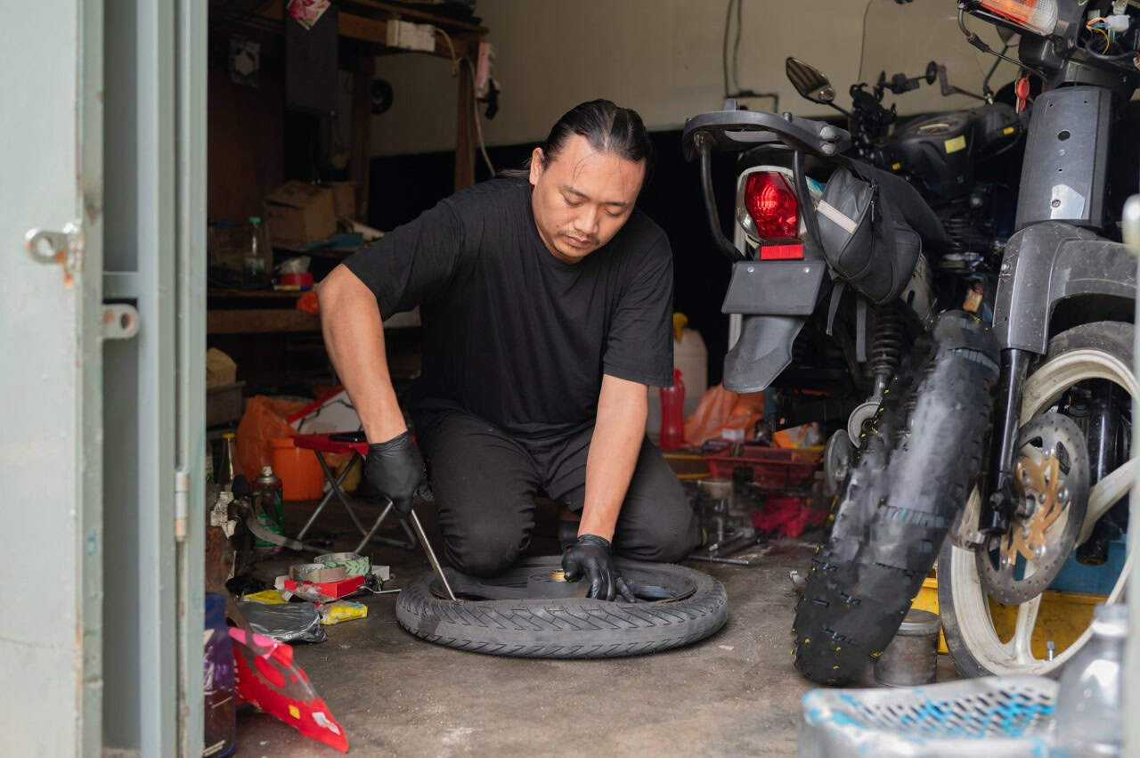 Man practicing motorcycle tire changing with hand tools in a garage, learning proper technique through repetition.