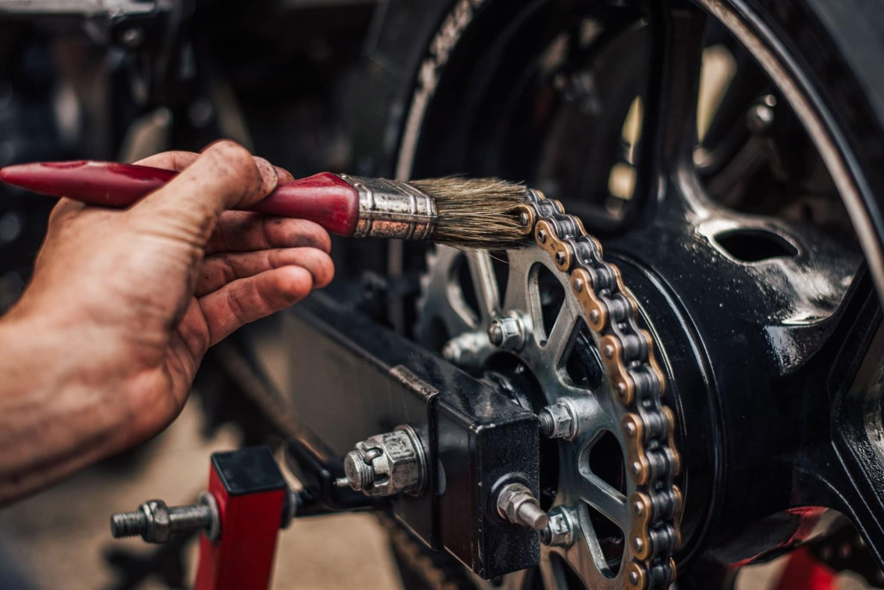 Person cleaning motorcycle chain with a brush during maintenance