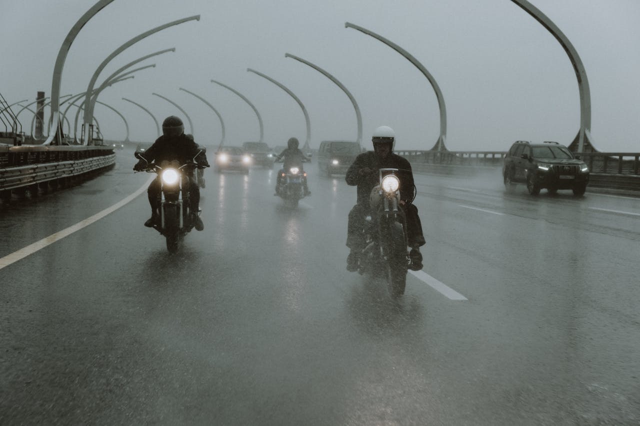 Group of motorcyclists riding through heavy rain on a bridge, illustrating the importance of waterproof riding gear