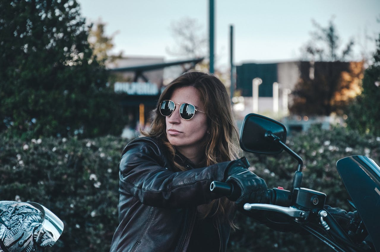Woman in a leather jacket and sunglasses sitting on a motorcycle, embodying confidence and personal style on and off the bike.