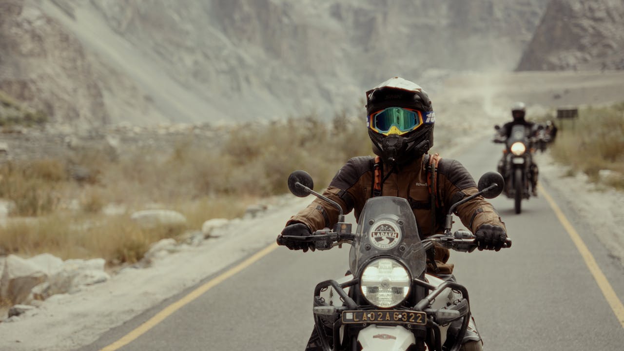 Adventure motorcyclist wearing goggles and helmet riding through a rocky mountain road with friends in the background