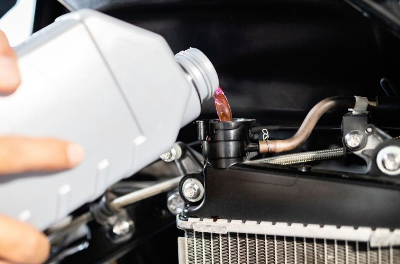 Pouring motorcycle coolant into a radiator during maintenance close-up