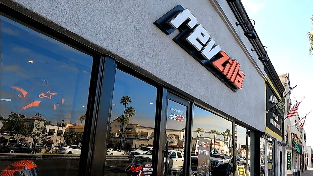 RevZilla retail store exterior with logo signage and motorcycles visible through the window.