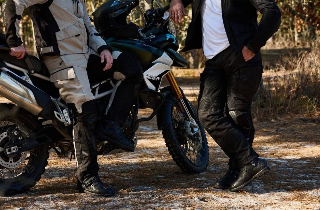 Two riders wearing Sedici Marco 2 Mesh Waterproof Pants resting beside an adventure motorcycle on a forest trail.