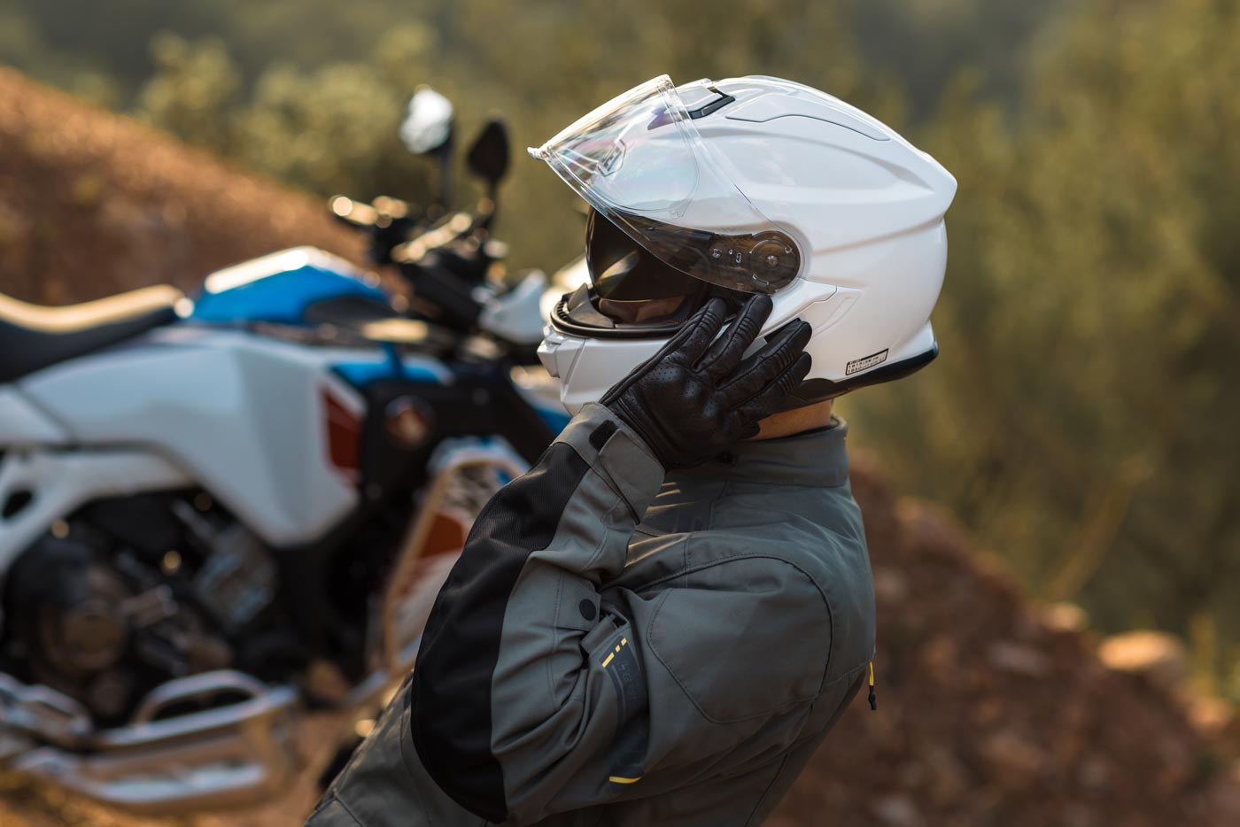 Rider adjusting a white Shoei GT-Air 3 helmet before a ride, showcasing its sleek touring design and aerodynamic shell