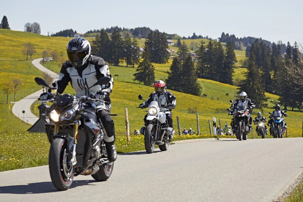 Group of motorcyclists riding together through scenic countryside hills, communicating with helmet intercoms to stay connected.