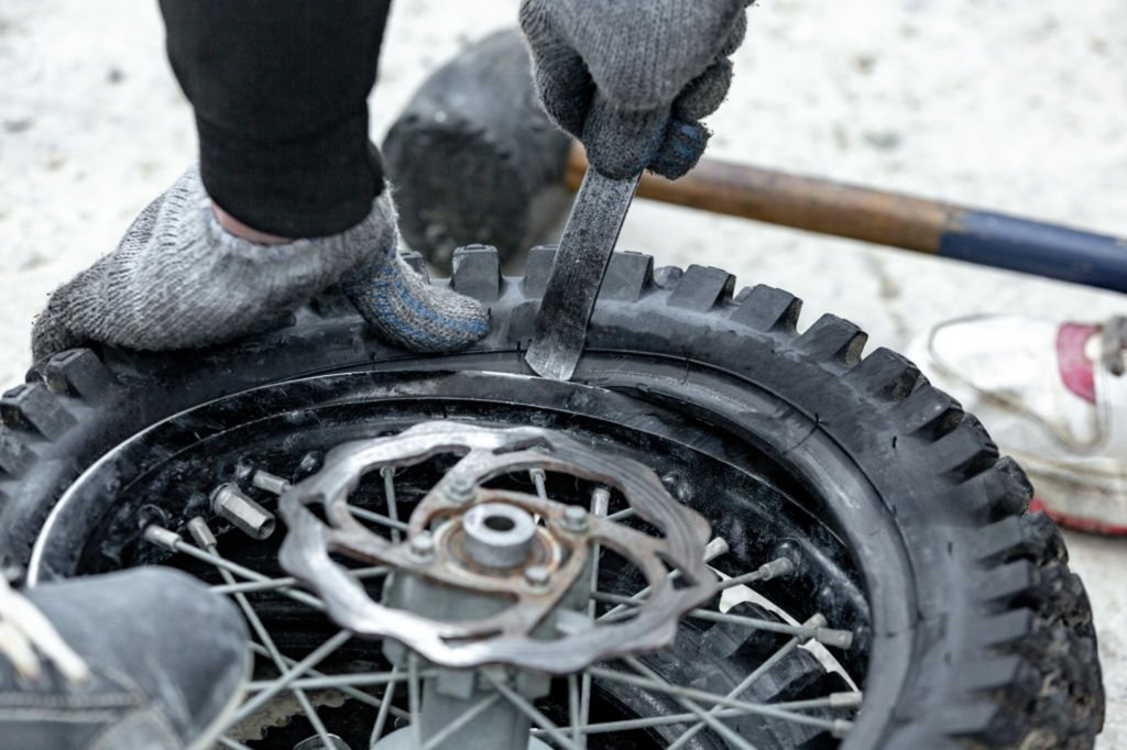 Close-up of a rider using tire irons to remove a dirt bike tire from the rim during a manual tire change.