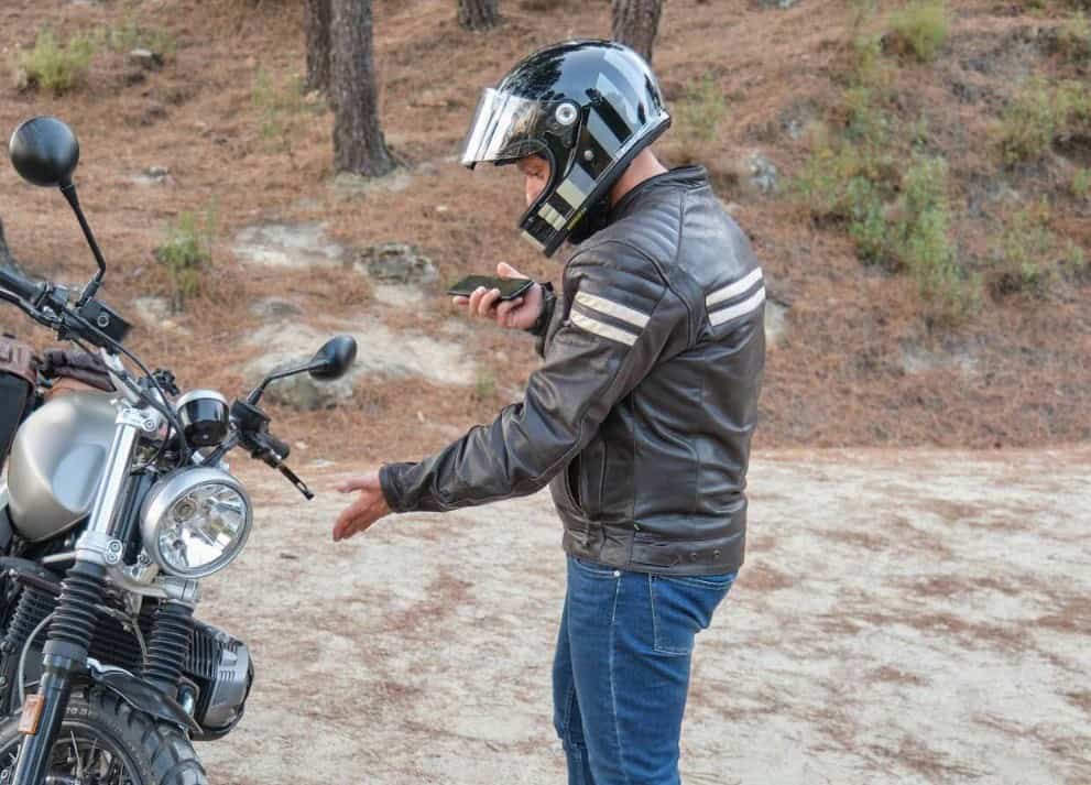 Motorcyclist calling for roadside assistance beside a stalled bike on a forest road