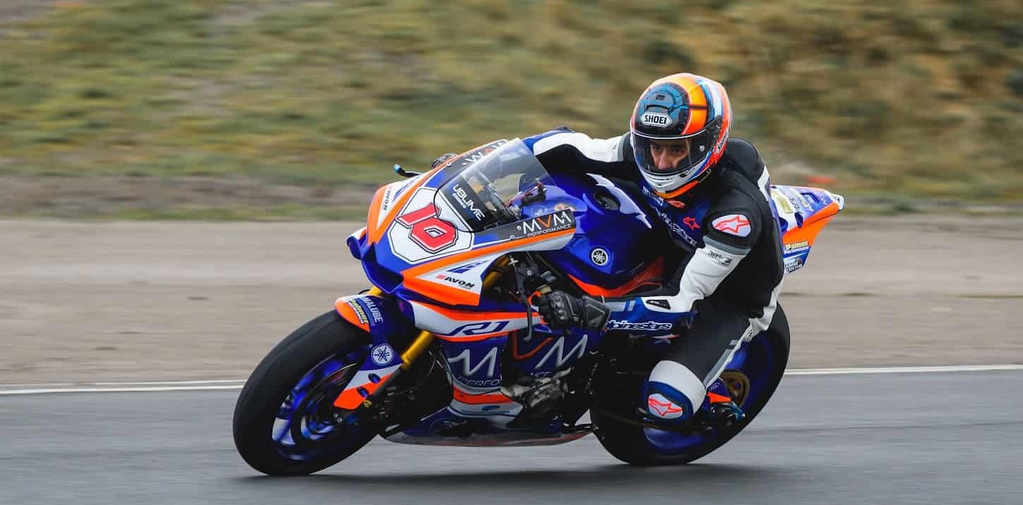 Motorcyclist in full racing gear leaning into a turn on a blue and orange sport bike during a track ride.