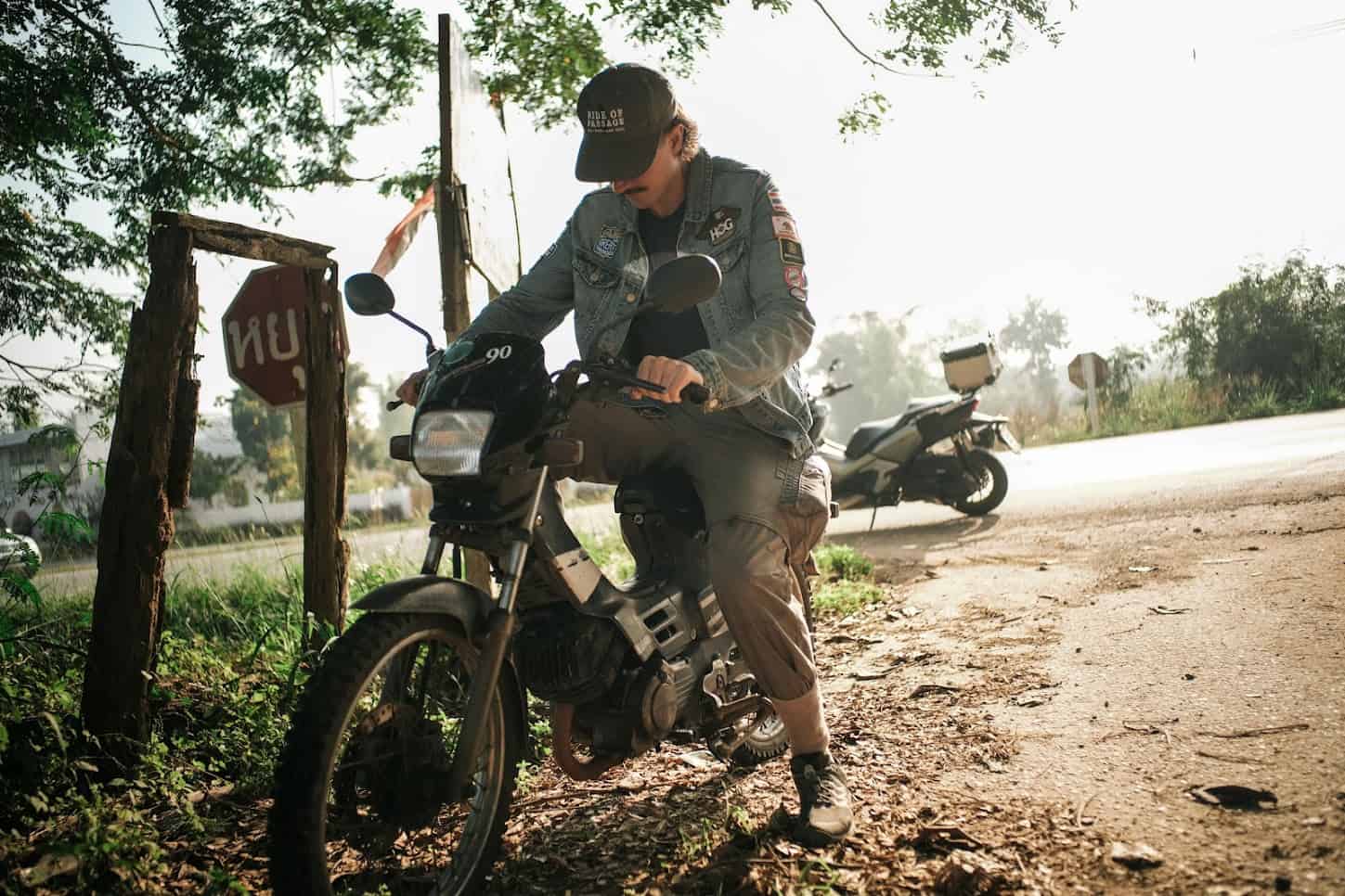 Rider on an old motorcycle parked roadside under morning light