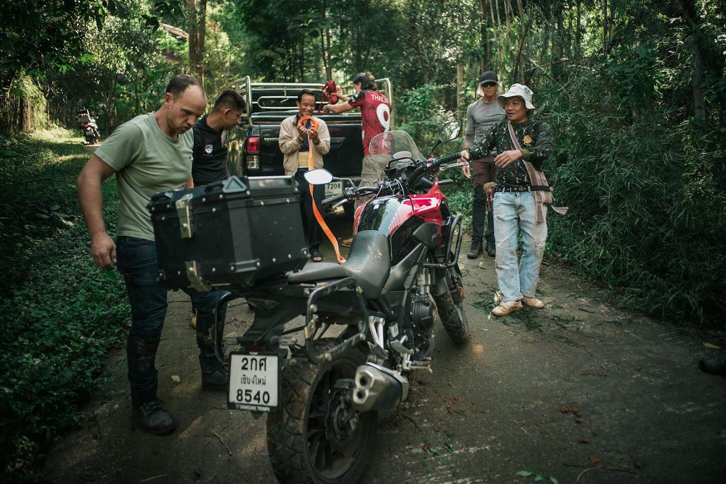 Group of riders assisting with a motorcycle breakdown on a forest road