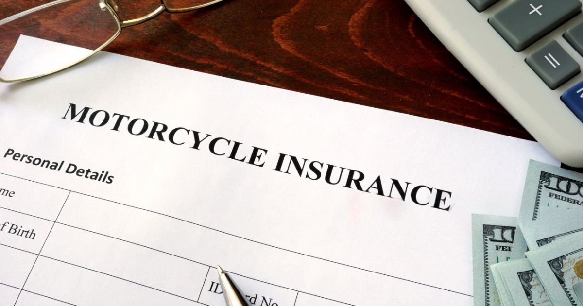 Motorcycle insurance form on a desk with money, glasses, and calculator