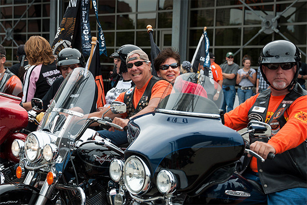 Group of smiling Harley riders at a motorcycle club event, symbolizing the perks and community benefits of rider associations.