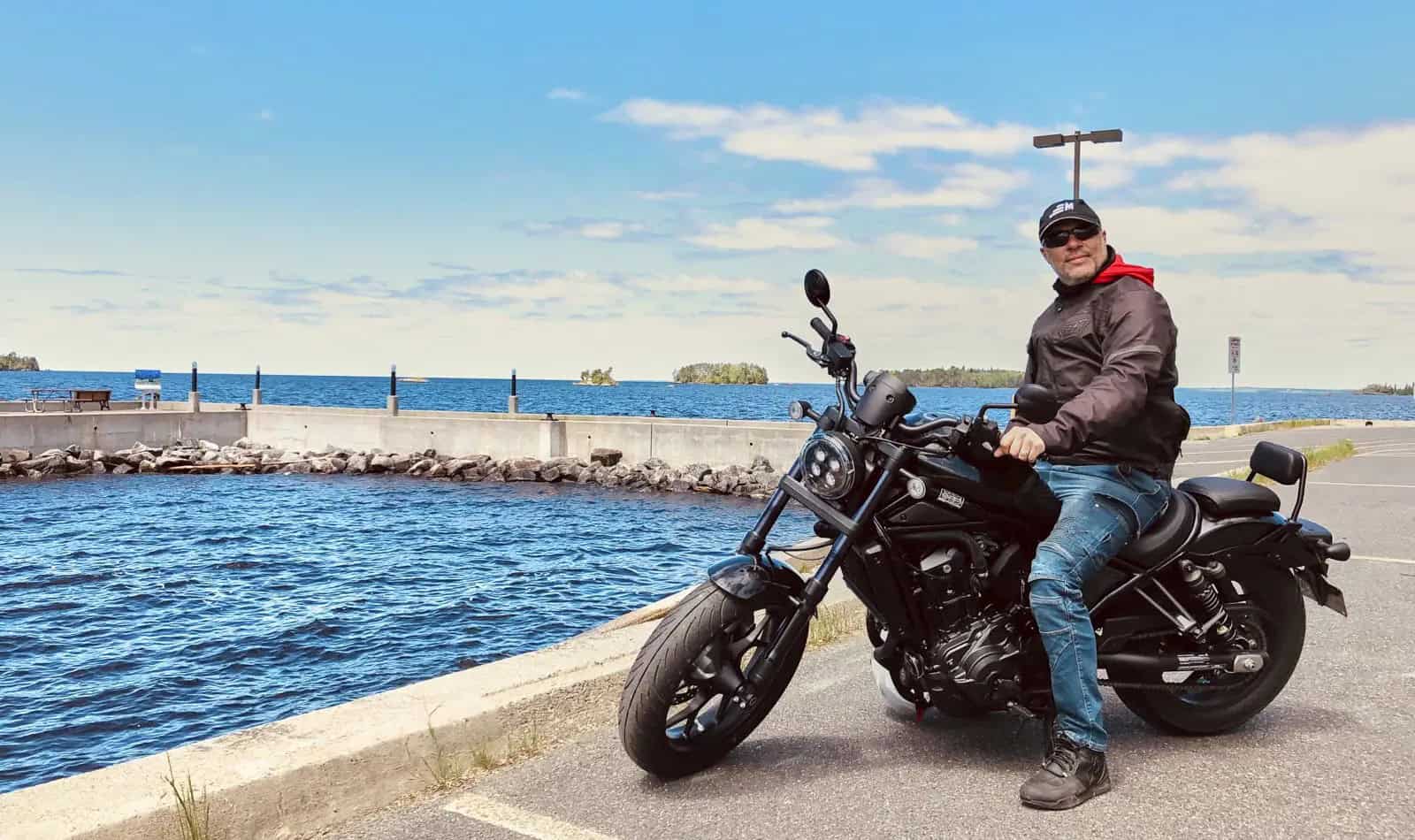 Rider on a black motorcycle by a lakeside dock on a clear day