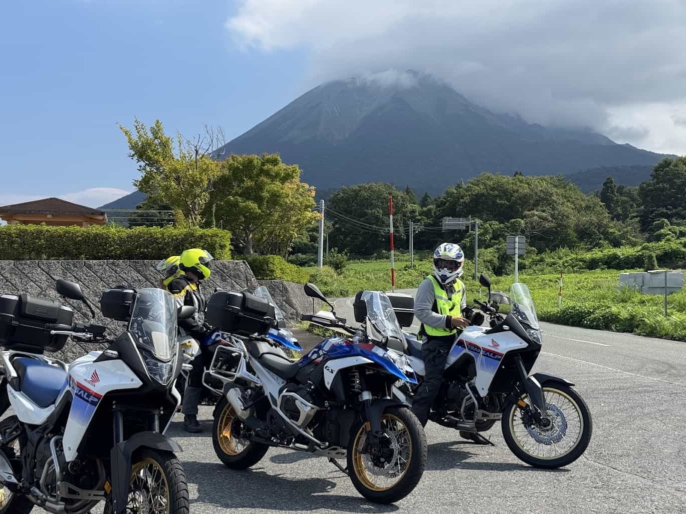 Adventure riders on dual-sport motorcycles parked with mountain scenery in the background
