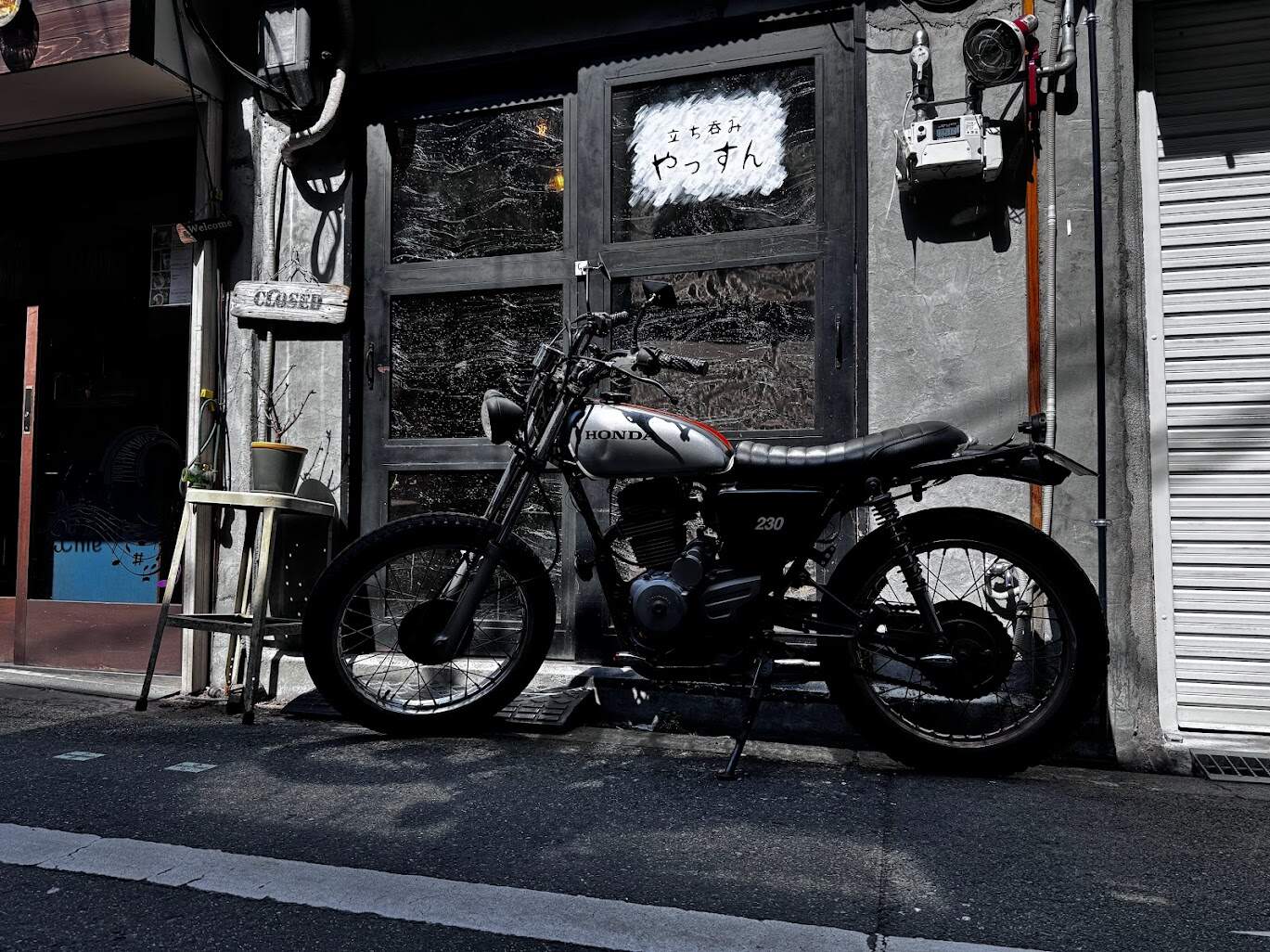 Honda 230 motorcycle parked on a quiet city street outside a shop