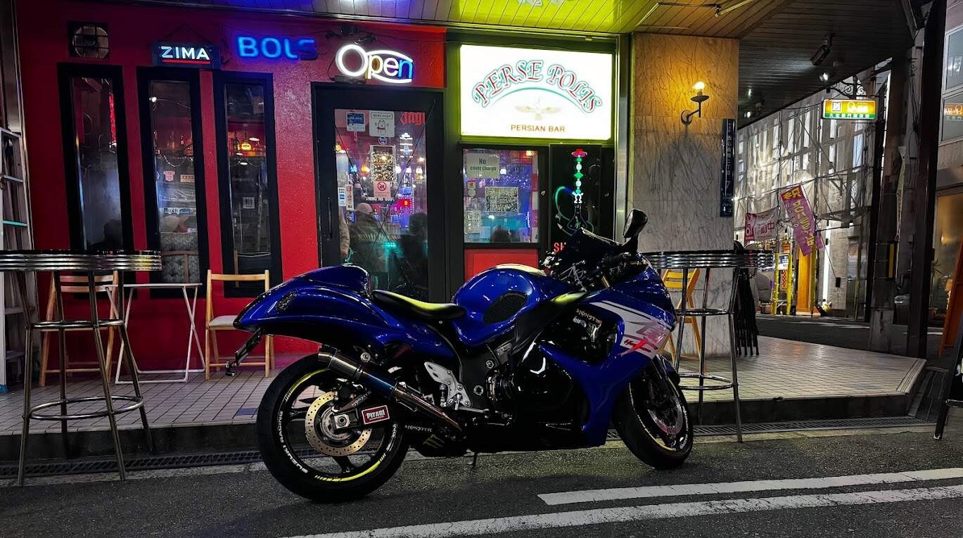 Blue sportbike parked outside a city bar at night with neon lights